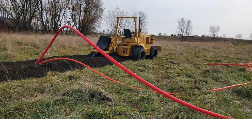 Trencher laying orange conduit across a field